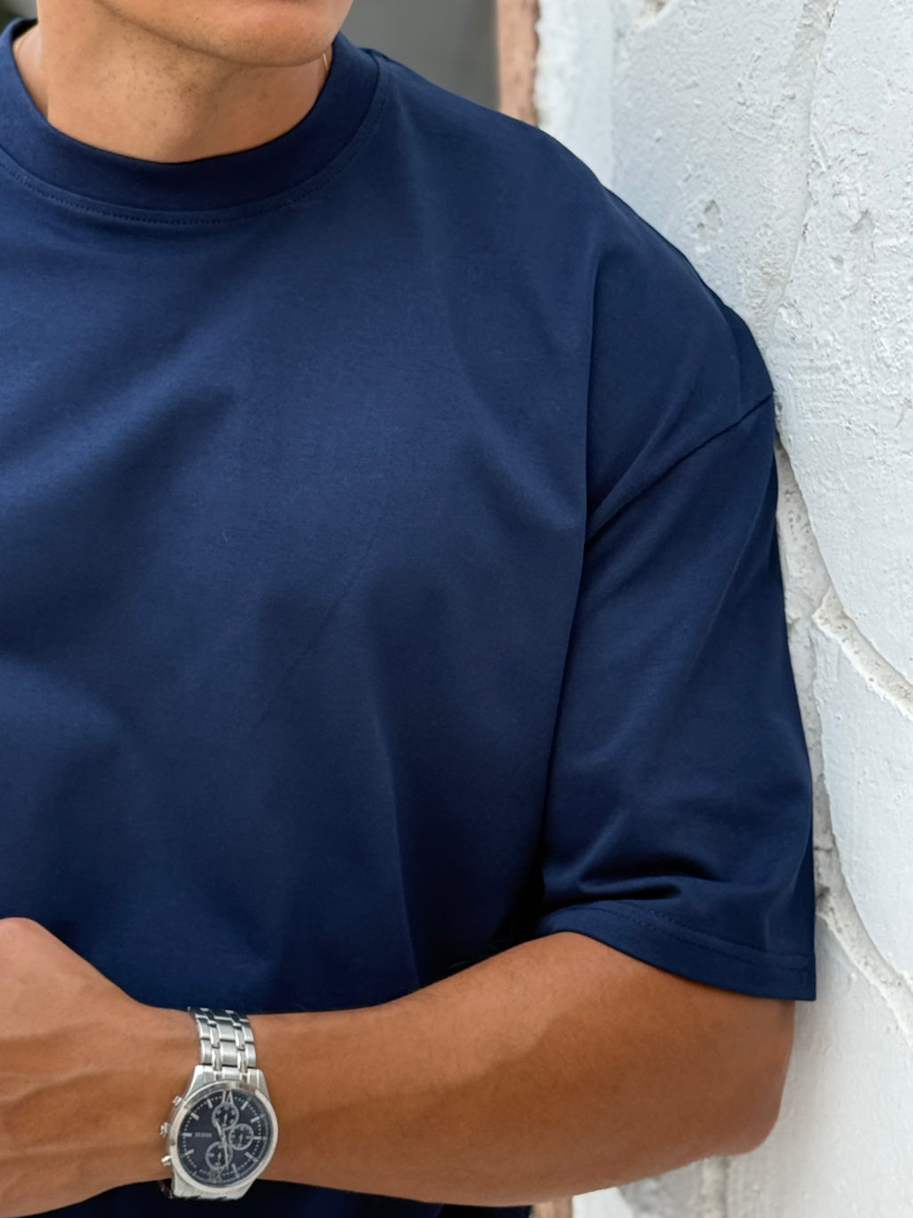 man, wear t-shirt white cotton, fame clothes A man wearing a black cotton t-shirt, white shorts, and beige sandals stands in front of a white textured stucco building with arched windows. From fame clothes 